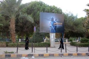 HVERDAGEN I BYEN: Kvinner i niqab går her forbi IS-propaganda i en park i Raqqa, 1. november 2014. På plakaten står det, grovt oversatt, at "vi skal vinne fram, tross den globale koallisjonen". Foto: Str / Rmc / AFP Photo / NTB Scanpix
