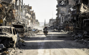 A Syrian youth uses his cellphone to film the destroyed vehicles and heavily damaged buildings down a street in Raqqa on Oct. 20, 2017, after a Kurdish-led force expelled ISIS fighters from the northern Syrian city, formerly the group's "capital." Bulent Kilic/AFP/Getty Images