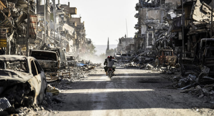A Syrian youth uses his cellphone to film the destroyed vehicles and heavily damaged buildings down a street in Raqqa on Oct. 20, 2017, after a Kurdish-led force expelled ISIS fighters from the northern Syrian city, formerly the group's "capital." Bulent Kilic/AFP/Getty Images