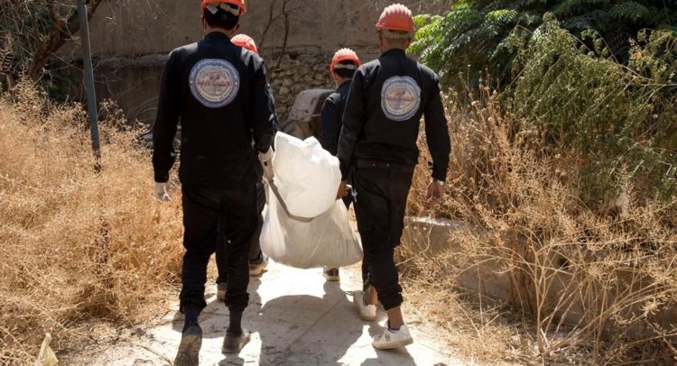 In this Saturday, Sept. 7, 2019 photo, first responders remove a body at the site of a mass grave in Raqqa, Syria. First responders said they have pulled nearly 20 bodies out of the latest mass grave uncovered in Raqqa, the Syrian city that was the de facto capital of the Islamic State group. It is the 16th mass grave in the city, and officials are struggling with a lack of resources needed to document and one day identify the thousands of dead who have been dug out. (AP Photo/Maya Alleruzzo)
